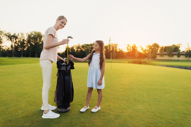 Mamá toma un club. Enseña a los niños a practicar golf. Pasatiempo familiar.