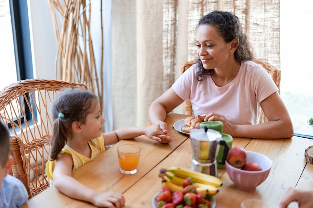Mamá toma la mano de su hija y escucha atentamente sus historias durante el desayuno familiar con frutas y croissants.
