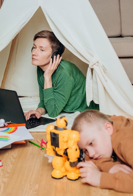 Mamá trabaja auriculares portátiles niño juega a continuación