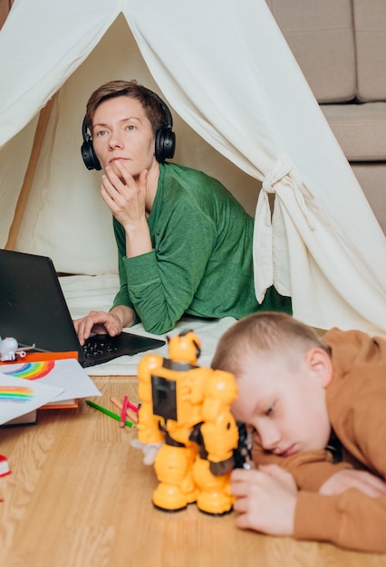 Mamá trabaja auriculares portátiles niño juega a continuación