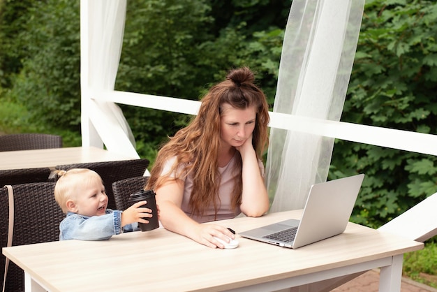 Mamá trabaja en una computadora portátil en un café, el niño interfiere con el trabajo y la comunicación, un lugar para copiar