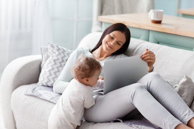 Mamá trabaja en una computadora portátil en casa mientras su hijo está jugando