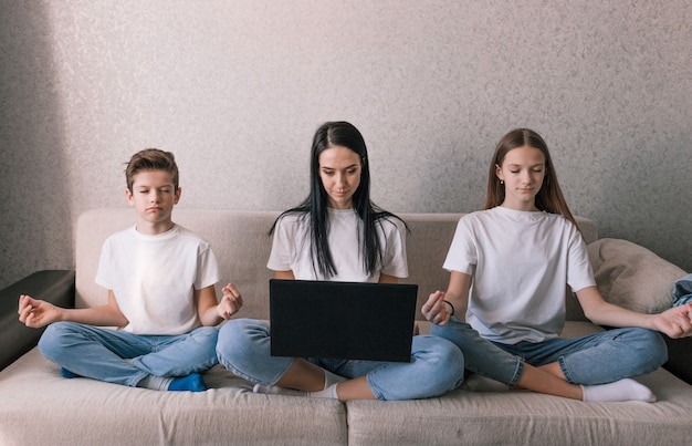 Mamá trabaja con entusiasmo en la computadora los niños meditan sentados uno al lado del otro en el sofá el concepto de trabajo y ocio