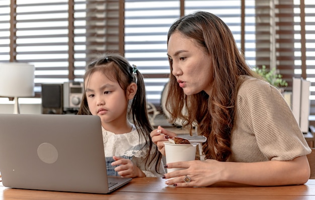 Mamá trabajando y enseñando a su hija para el aprendizaje en línea en casa. Estilo de vida de unión familiar y nueva normalidad después de Covid-19.