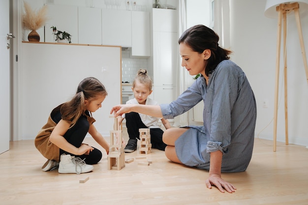 Mamá tranquila jugando con sus hijos en el piso Construyendo cosas con bloques de madera Usa maquillaje y ropa cómoda La niña tiene rabo