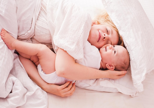 Mama umarmt Baby in Weiß und genießt den Morgen im Bett