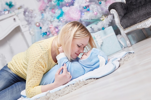 Mama umarmt ihr Baby in der Nähe des Weihnachtsbaums. das Konzept von Weihnachten