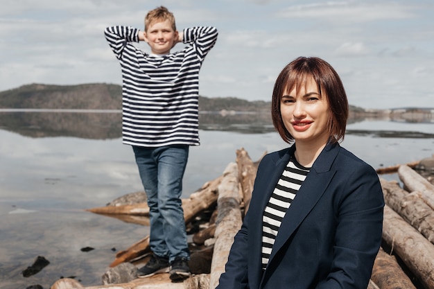 Foto mama umarmt ihren sohn am flussufer. eine schöne, moderne mutter mit einem glücklichen sohn in gestreiften westen.