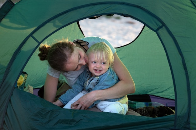 Mama umarmt kleines Kind im Touristenzelt auf dem Campingplatz. Aktive Erholung mit Kindern.