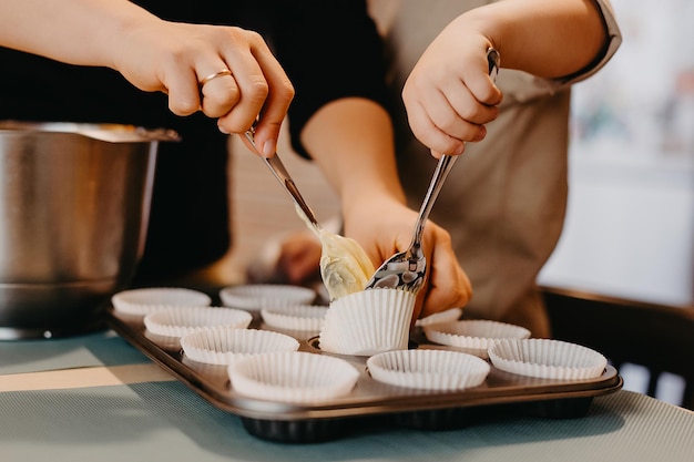 Mama und ihr Sohn helfen in der Küche beim Zubereiten von Cupcakes Der Junge mit Gips an der Hand mischt den Teig und legt ihn in Backformen und Mama erzählt