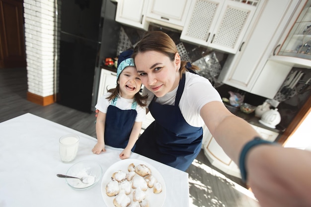 Mama und ihre Tochter backen zu Hause Kekse in der modernen Küche und machen Selfie