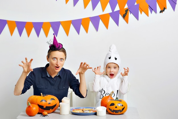 Mama und ihre Tochter machen wütende Gesichter, wenn sie Halloween feiern. Weißer Hintergrund mit farbigen Fahnen