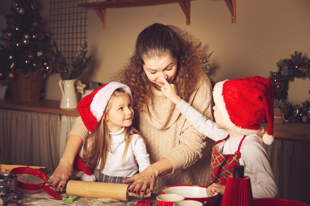 Mama und Kinder bereiten Kekse in der Küche zu. Weihnachtsdekorationen, Familientraditionen, Weihnachtsessen, Feiertagsabend.