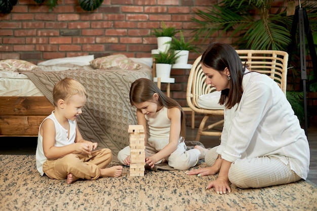 Mama und Kinder spielen Squirl Jenga Tower. Frau Mädchen und Junge spielen Familienpuzzlespiel. Familientag frei