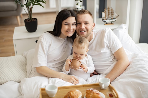 Mama und Papa genießen Brunch mit ihrer kleinen Tochter im Bett