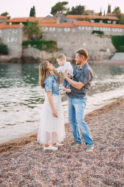 Mama und Papa halten ihren kleinen Sohn vor dem Hintergrund der Sveti am Meer in den Armen