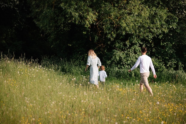 Mama und Papa machen mit ihrem 3-jährigen Sohn einen Spaziergang durch Wald und Feld mit blühenden Wiesen