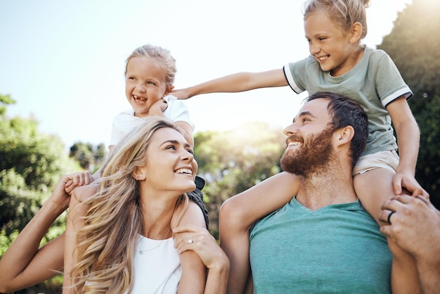 Mama und Papa mit Kindern auf der Schulter im Garten spielen zusammen Lieben Sie junge und glückliche Familienbande und haben Sie Spaß in einem Park an einem Sommertag Vater, Mutter und Töchter genießen es, in der Natur zu sein