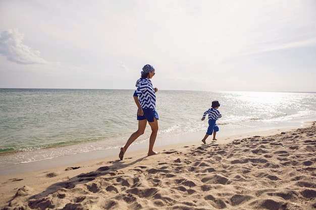 Mama und Sohn in blauer Kleidung laufen im Sommer im Urlaub ans Strand Meer