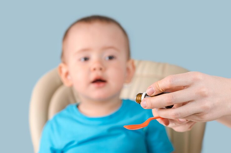 Mamá vierte el jarabe con el medicamento en una cuchara, el niño mira con curiosidad la cuchara con vitaminas.