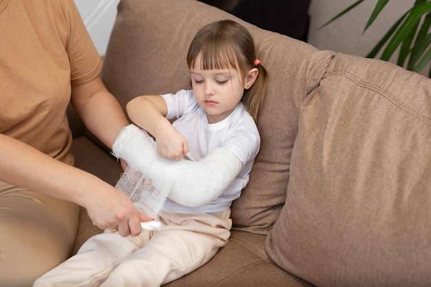 Mama wickelt einen Verband um den gebrochenen Arm ihrer Tochter Gips