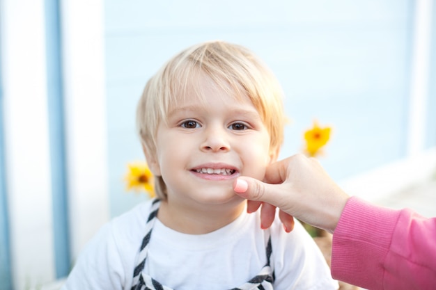 Mama wischt einem kleinen Jungen das Gesicht ab. Säuglingspflege. Porträt eines lächelnden blonden kleinen Jungen. Das Konzept einer glücklichen Familie und Elternschaft. Kindheitskonzept. Das Kind wurde beim Spielen auf dem Hof schmutzig