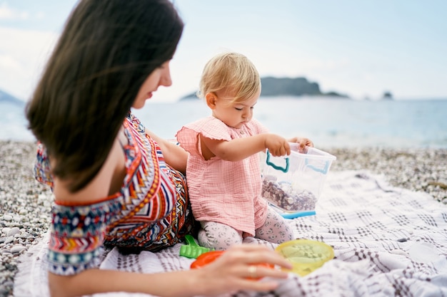 Mamá yace sobre una manta en una playa de guijarros junto a una niña sentada