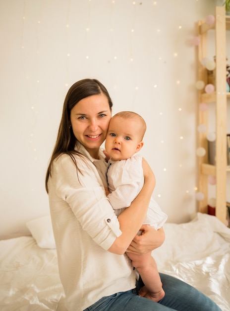 Mamãe abraça sua filha bebê sentada na cama