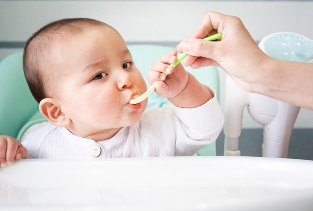 Mamãe alimenta o bebê com uma colher de purê de legumes na mesa de alimentação das crianças apetite do bebê nutrição saudável introdução de alimentos complementares copyspace mock up