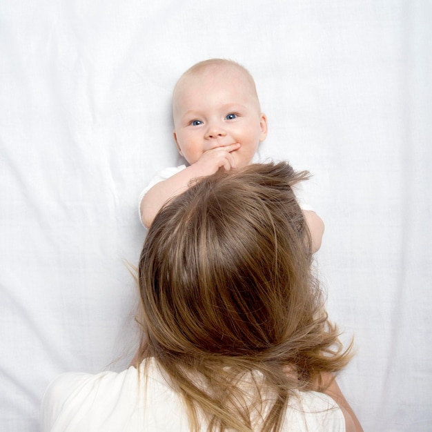 Mamãe brinca com um bebezinho na cama com um lençol branco. Camada plana, vista superior.