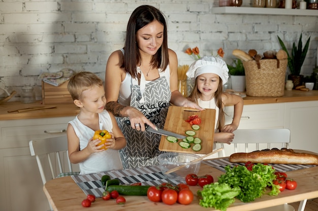 Mamãe cozinha o almoço com as crianças. uma mulher ensina sua filha a cozinhar com seu filho. vegetarianismo e alimentação natural saudável