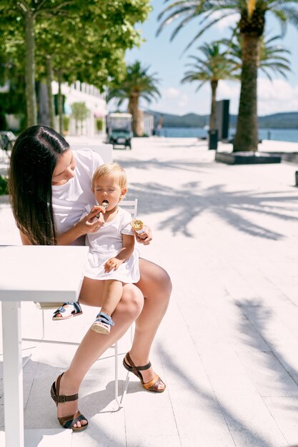 Mamãe dá sorvete para uma menina sentada em seu colo em um café