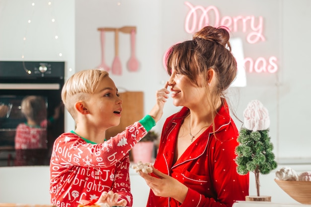 Mamãe e bebê felizes brincando e assando biscoitos na cozinha para o Natal