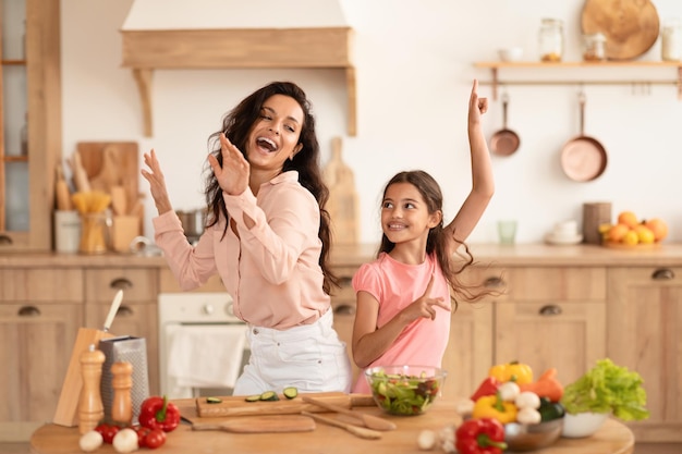 Mamãe e filha brincando preparando o jantar juntas dançando na cozinha