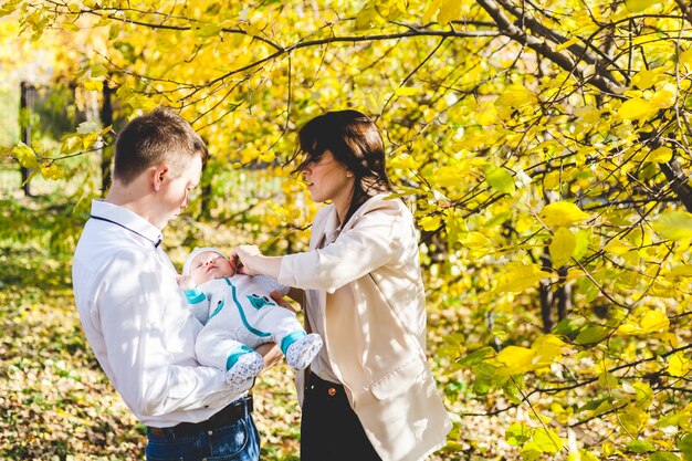 Mamãe e papai com um bebê, um garotinho andando no outono no parque ou na floresta. folhas amarelas, a beleza da natureza. comunicação entre um filho e um pai.