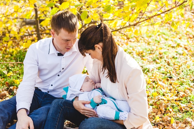 Mamãe e papai com um bebê, um garotinho andando no outono no parque ou na floresta. Folhas amarelas, a beleza da natureza. Comunicação entre um filho e um pai.