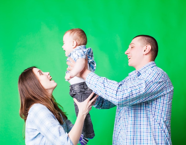 Mamãe e papai felizes brincam com um lindo bebê sorridente. Emoções humanas positivas, fundo verde.