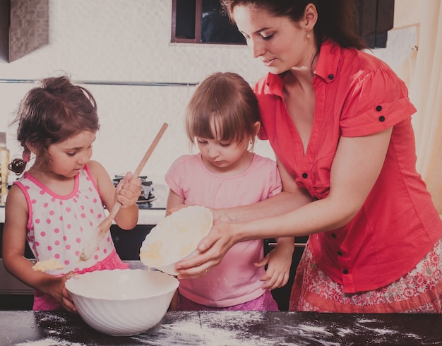 Mamãe está fazendo biscoitos com os filhos na cozinha de casa