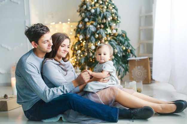 Mamãe, papai e bebê se abraçam e se alegram na noite de inverno do Natal perto da árvore do ano novo