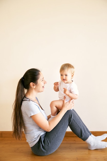 Mamãe se senta no chão e segura um bebezinho no colo