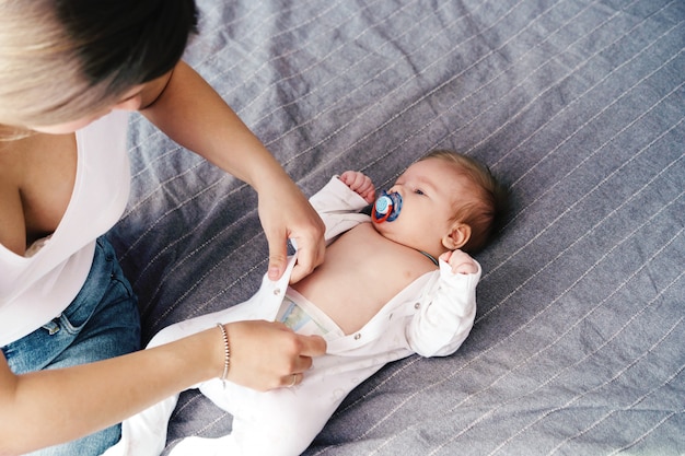 Mamãe veste um bebê recém-nascido, abotoando um macacão.