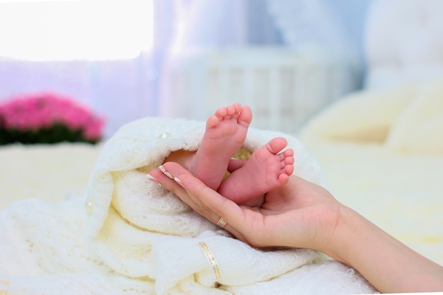 Mamas Hände halten die kleinen Beine ihres Neugeborenen, eingehüllt in eine weiße warme Decke