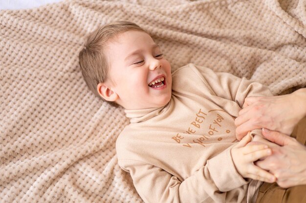 Mamas Hände kitzeln kleines Baby, lacht und hat Spaß mit Mama zu Hause auf dem Bett