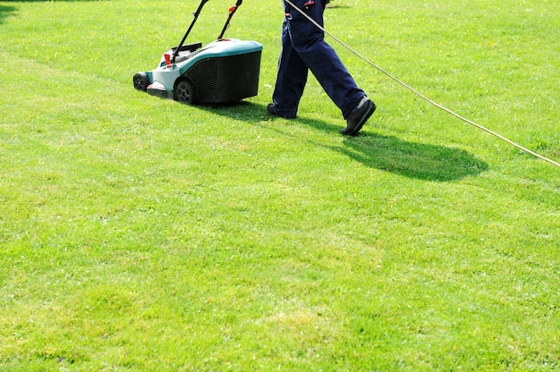 Man bewegt sich mit Rasenmäher &amp; mäht grünes Gras