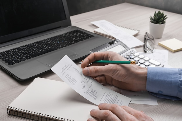 Man Hand mit Taschenrechner und Schreiben notieren mit berechnen über Kosten und Steuern im Home Office. Geschäftsmann, der einige Papiere am Arbeitsplatz erledigt