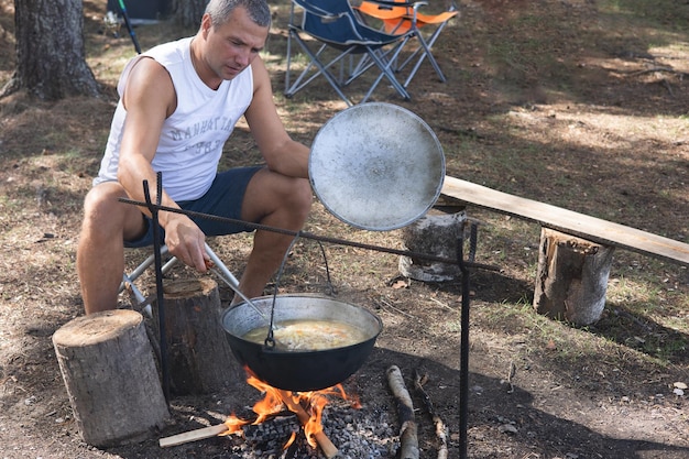 Man kocht im Kessel auf offenem Feuer in der Natur Topf am Lagerfeuer auf dem Hintergrund des Waldes Campingleben Reisen vor Ort