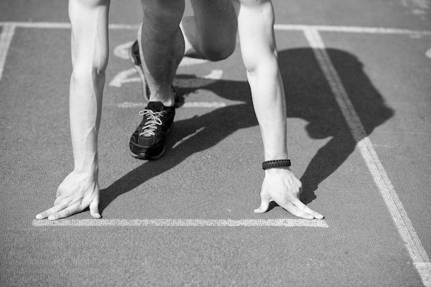 Man Läufer athletischer Typ mit muskulösen Händen und Beinen starten auf Laufbahn oder Laufband in schwarzen Modeschuhen sonnige Outdoor-Sommeraktivität und sportliche Herausforderung für einen gesunden Lebensstil