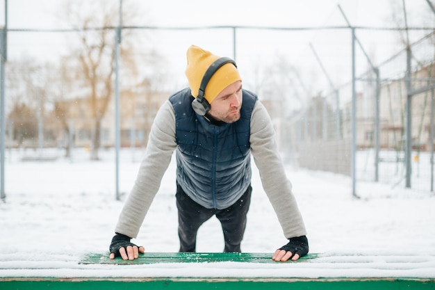 Man sieht einen jungen und fitten erwachsenen Mann, der beim winterlichen Outdoor-Gymnastik an seine Grenzen geht