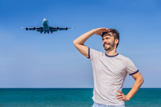 Man Tourist hat Spaß am Strand und beobachtet die landenden Flugzeuge, die auf einem Flugzeugkonzepttext reisen