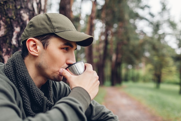 Man Tourist Reisender trinkt heißen Tee von Thermoskanne Tasse im Frühlingswald. Camping, Reisen, Wandern und Sportkonzept